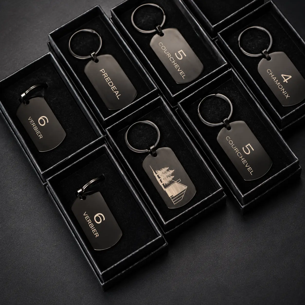 Brelocuri dog-tag negre gravate cu numele stațiunilor de schi și numărul camerei, în cutii negre